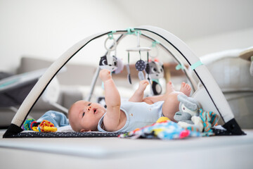 Cute baby boy playing with hanging toys arch on mat at home Baby activity and play center for early...