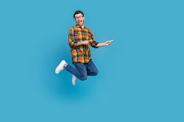 Full body portrait of excited cheerful man jump indicate fingers empty space isolated on blue color background