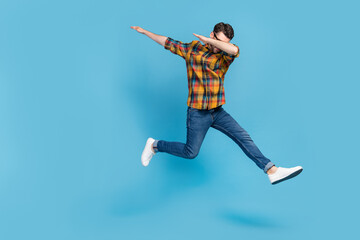 Full body portrait of overjoyed young man jumping arms dabbing isolated on blue color background
