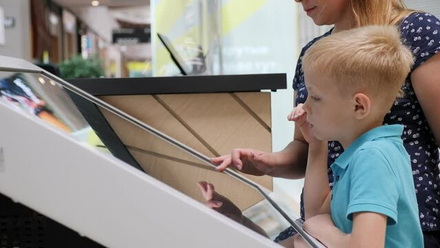 Close-up of a woman with a child standing near a large screen in a shopping center and clicking on the screen. A plan of the shopping center on a large touch screen.