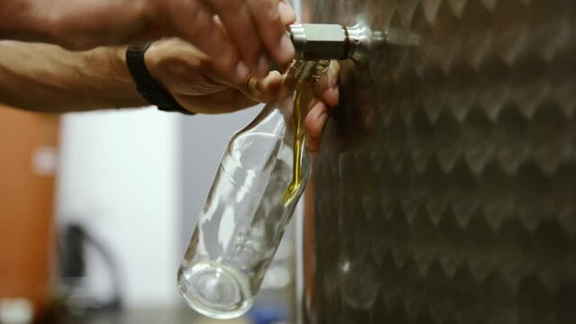 Un main tourne le robinet d'une cuve pour remplir une bouteille en verre d'huile d'olive