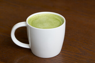 Cup of hot green tea latte on the wooden table.