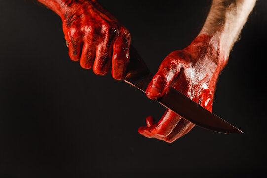A man wipes a bloody knife with his hand on a black background. 