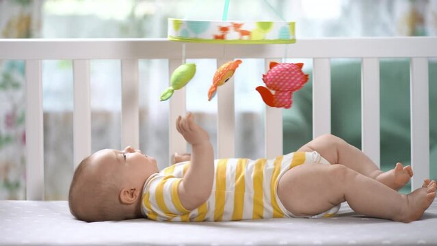 The three month baby in the crib looking at the mobile carousel and smiling. Happy child. Newborn is in the crib. Mobile for children.