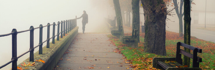 Young woman walking alone down the alley in autumn mist
