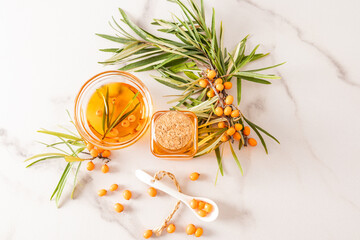 Plakat top view of a glass bottle with a lid and a bowl filled with organic sea buckthorn oil. twigs and berries on a marble background. a vitamins.