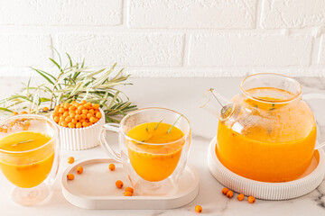 tea party ceremony in cold weather. healthy sea buckthorn tea in two glass cups and a teapot on a white marble table opposite the brick wall.