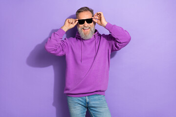 Portrait of handsome retired positive man with white gray beard wear purple hoodie hold sunglass...