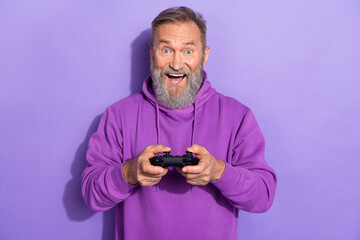 Portrait of retired cheerful impressed man dressed purple hoodie holding joystick play station...