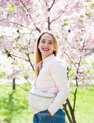 portrait of a smiling blonde woman in spring park in pink blossoming sakura 