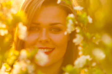 Young smiling woman in orchard full of flowers on a sunny spring day