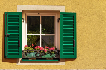 Fototapeta na wymiar Close-up of a window with green wooden shutters and red geranium flowers. Small village of Malborghetto-Valbruna in Val Canale, Udine province, Friuli-Venezia Giulia, Italy, Europe.
