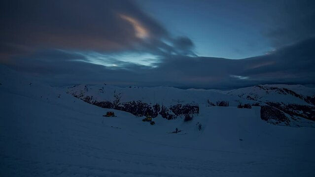 Building a snow castle sculpture with heavy equipment at twilight in the Alps - time lapse