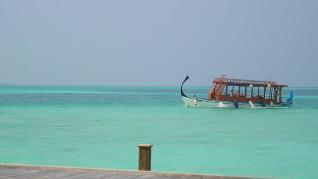 Traditional Wooden Maldivian Boat coming into dock across turquoise blue water