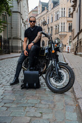 Fototapeta na wymiar Portrait of attractive man biker with tattooes posing on his motorcyle in alleyway downtown.