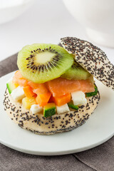 A gourmet sandwich with poppy seeds, salmon, kiwi, fresh cheese and vegetables.