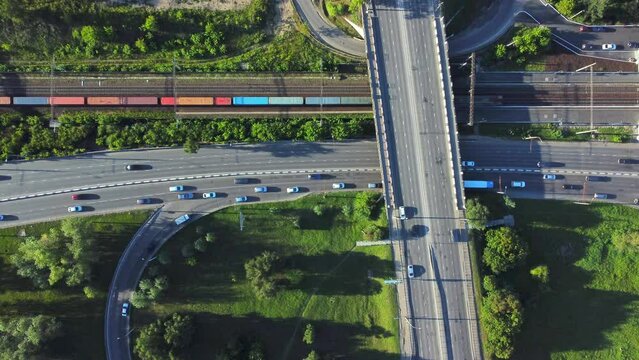 4k Aerial view of cars drive along road and railroad in countryside irrl. Top pic of lot of transport riding on intersecting express way, moving trains and green trees outdoors. Operator uses drone