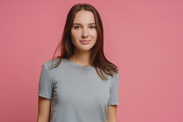 Adorable millennial girl with straight dark hair, wears casual t shirt, looks seriously at camera,...