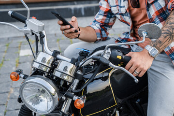 Portrait of trendy guy motorcyclist with smartphone riding motorbike outdoors.