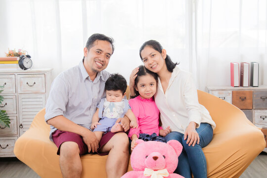 Selective focus Asian happy family sitting on cozy sofa cuddling with two little children take a photo in living room. Sibling with mom and dad spend time together in holiday, family enjoy free time.