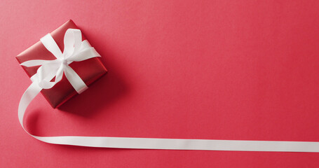 Image of red christmas gift with white ribbon and copy space on red background