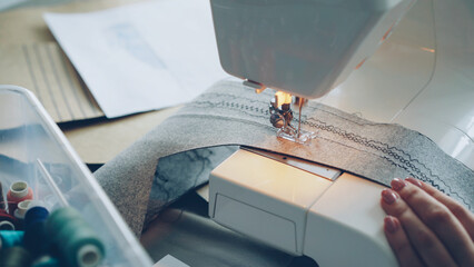 Close-up of modern electric sewing machine working stitching piece of textile. Girl's manicured...