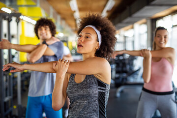 Fototapeta na wymiar Group of fit people working out in a gym. Multiracial friends exercising together in fitness club.