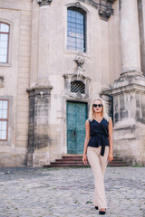 Fototapeta na wymiar A young, slender blonde in beige pants and a black blouse walks the old streets of Lviv. Ukraine.