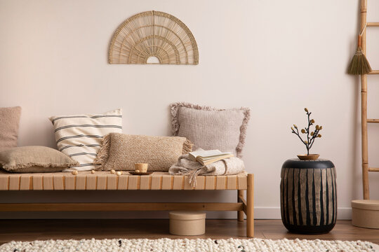 Creative composition of meditation living room interior with beige sofa, pillow, coffee table , decoration, ladder and personal accessories. Boho home decor. Template. 