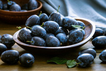 Ripe blue Fresh organic  sweet plums just picked from the tree, walnut wood bowl plate indoors. Autumn Harvest of fruits  rustic  wooden dark black background leaf clay.