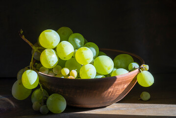 organic ripe seedless green grape clay ceramic dish bowl pot  wooden table Still life Close up rustic orange blue light.
