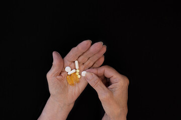 An elderly woman chooses which pill to take, hands on a black background