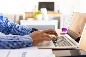 Hands of senior biracial businessman using laptop sitting at desk at home