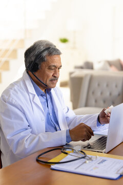 Vertical image of senior biracial male doctor using laptop and headset for video consultation