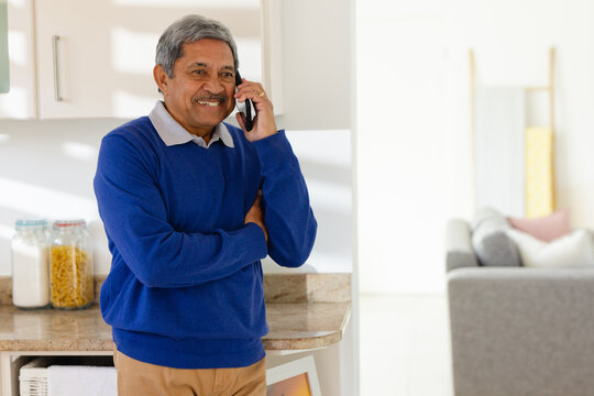 Smiling senior biracial man talking on smartphone in kitchen at home