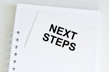 white card with text next steps lies on a notebook on a desk, a business concept