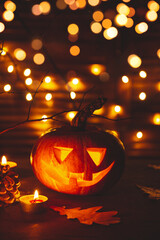 A Halloween pumpkin with a carved face and burning candles glows in the dark. Halloween card with pumpkin and beautiful bokeh, vertical photo