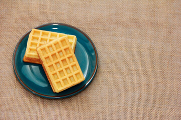 sweet baked fluted Belgian waffles on a blue ceramic plate and a baggy background
