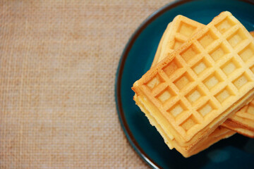sweet baked fluted Belgian waffles on a blue ceramic plate and a baggy background