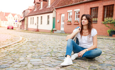 A sad and tired young woman sits on a stone road, she props her head with her hands, a frustrated woman is tired of everyday life and life, she wants rest and happiness.
