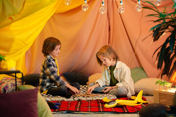 Two young boys which are similar in age are playing inside an indoor tent and messing around with a...