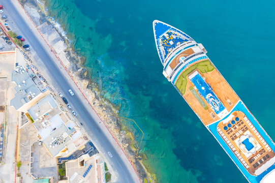 Cruise liner moored next to the turquoise sea embankment in the bay of the city, aerial top view.