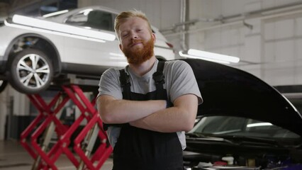 Portrait of a smiling successful car mechanic in a clean uniform with crossed arms against the background of modern cars at a service station - Powered by Adobe