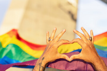 Hands making heart sign in front of rainbow flag..