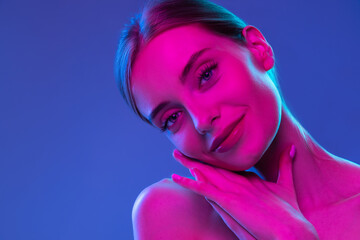 Neon glow. Young adorable girl with well-kept skin and naked shoulders isolated over dark background in pink neon light. Concept of art, fashion, style, inspiration