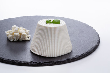 whole ricotta cheese on a black stone cutting board resting on a white background