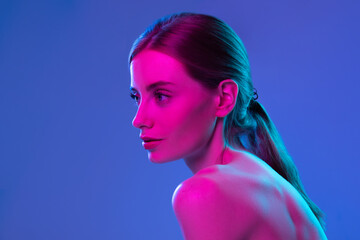 Neon glow. Young adorable girl with well-kept skin and naked shoulders isolated over dark background in pink neon light. Concept of art, fashion, style, inspiration