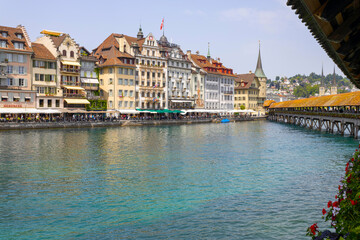 Naklejka premium LUCERNE, SWITZERLAND, JUNE 21, 2022 - View of the wodden covered Kapellbrücke Bridge on the Reuss river and buildings in city center of Lucerne, Switzerland