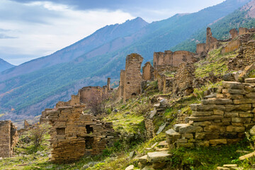 Fototapeta na wymiar Ruins and towers of the abandoned village of Goor, Dagestan, Russia. Stone towers on the background of blue sky on the emerald hills. Panoramic view of the ancient Goor settlement among the mountains