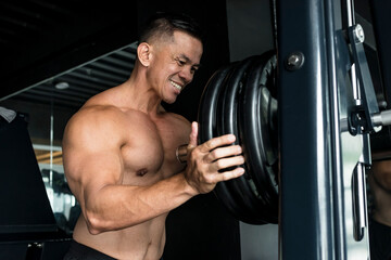 Fototapeta na wymiar Gritty scene of a brawny man ramming heavy barbell plates on a smith machine at the gym. Focus on rubberized black plates. Gym or Fitness club setting.